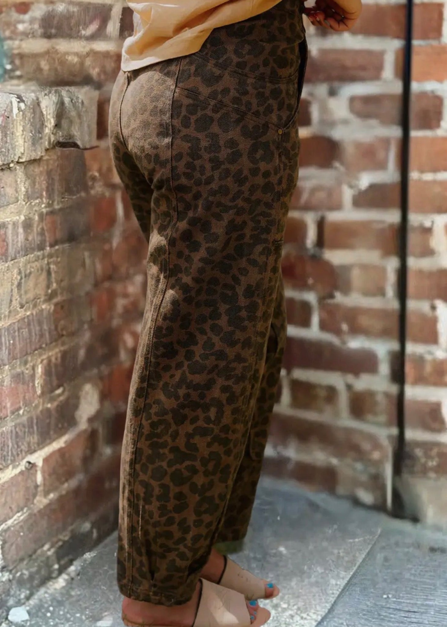 Person wearing leopard print pants against a brick wall.