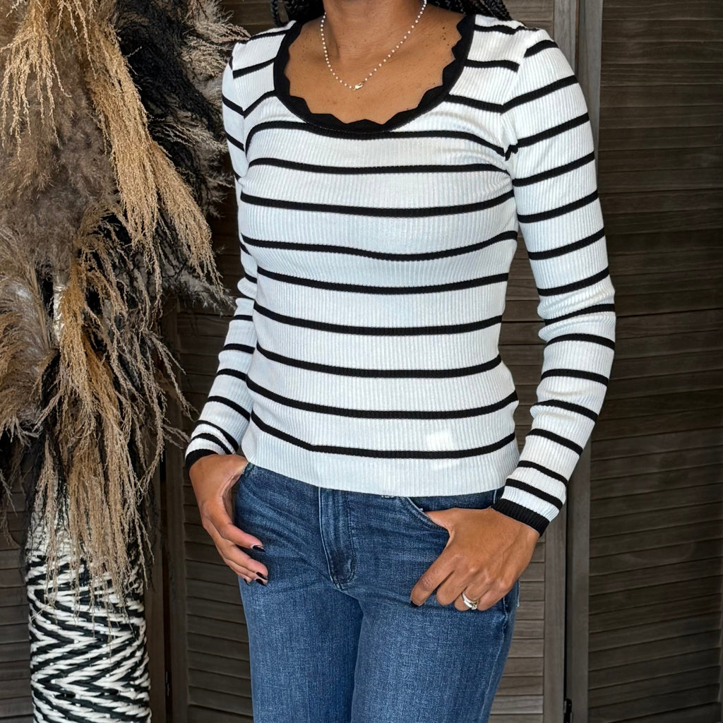Person wearing a black and white striped sweater and blue jeans standing against a neutral background.