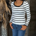 Person wearing a black and white striped sweater and blue jeans standing against a neutral background.
