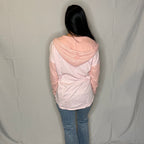 Person wearing a light pink and white jacket with blue jeans against a plain background