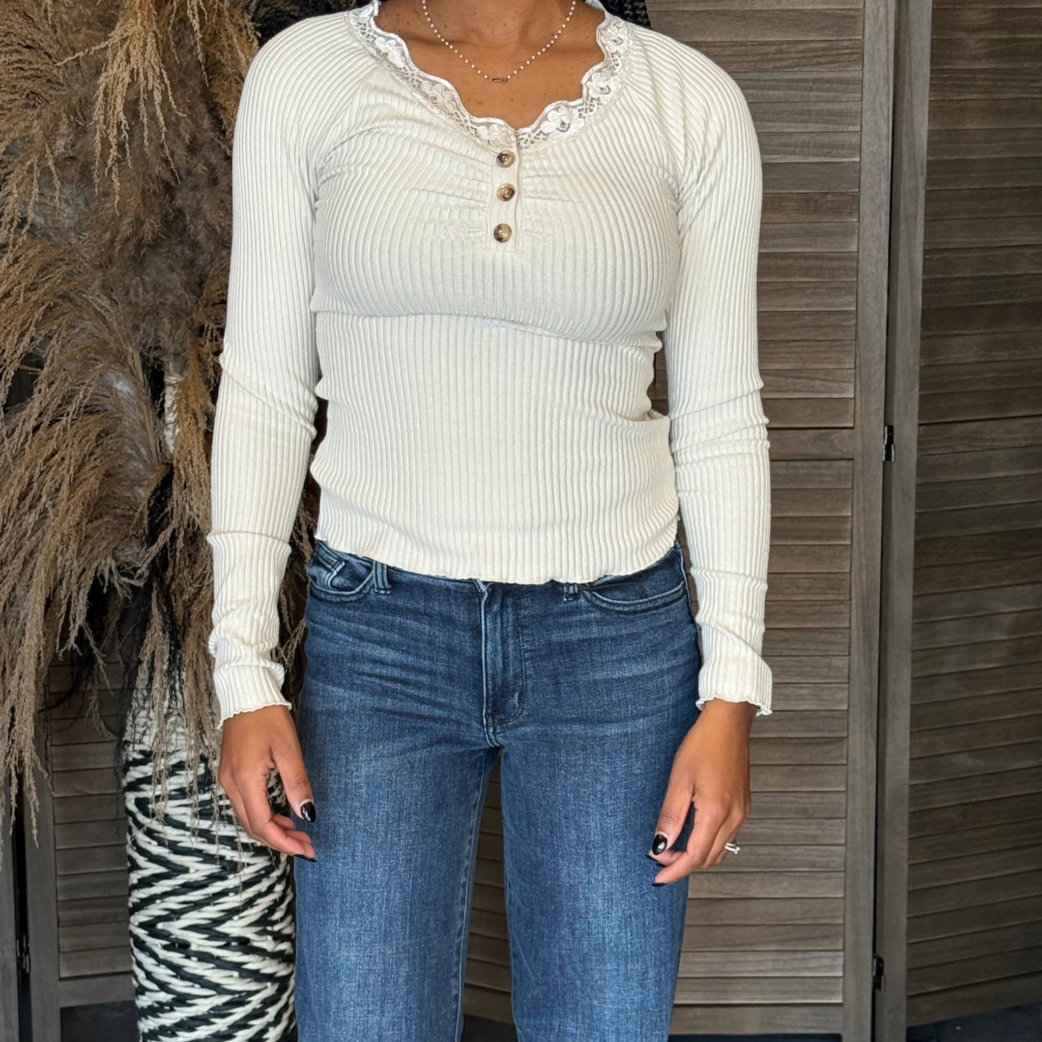 Person wearing a white long-sleeve top and blue jeans standing on a wooden deck.