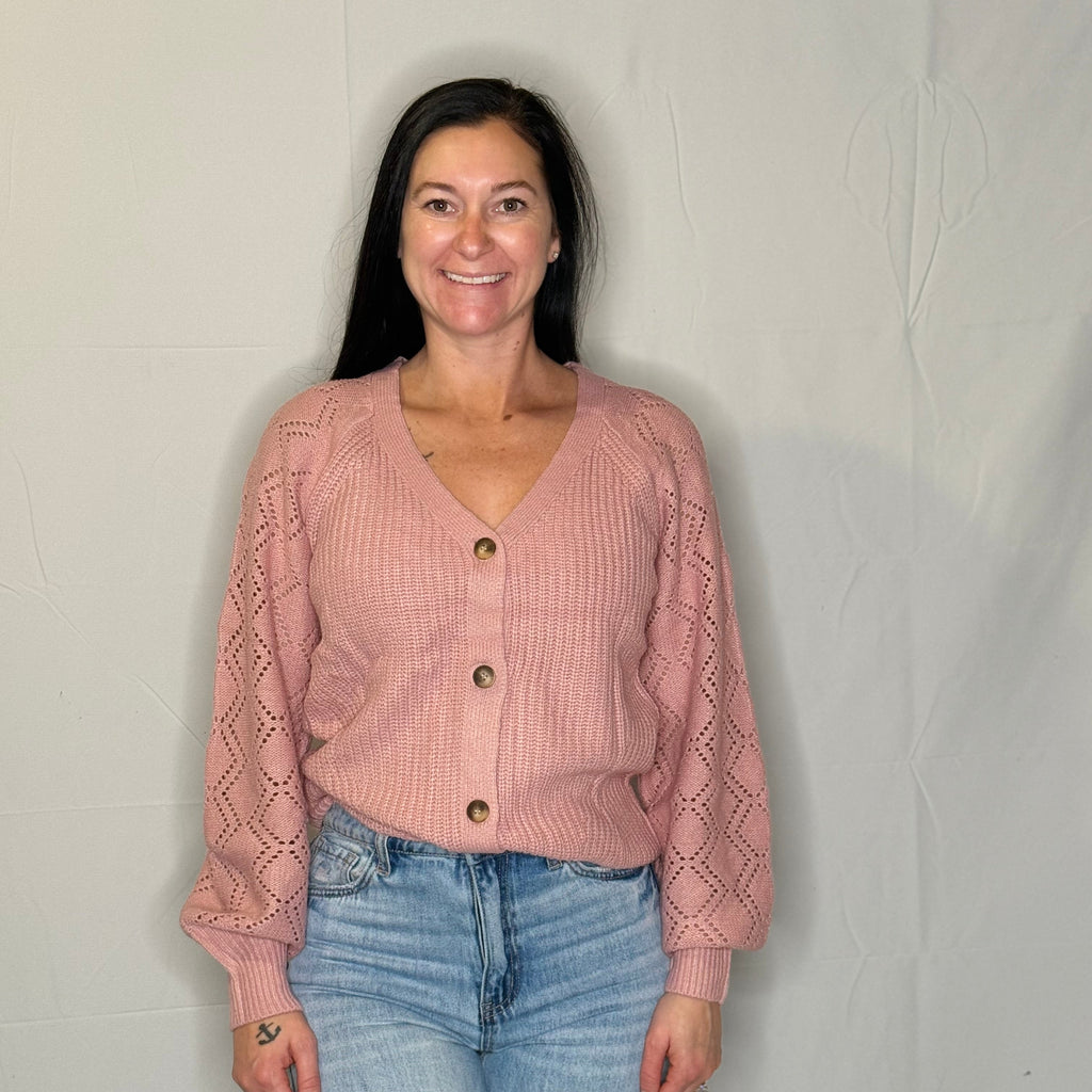 Woman wearing a pink knitted cardigan and blue jeans against a plain background