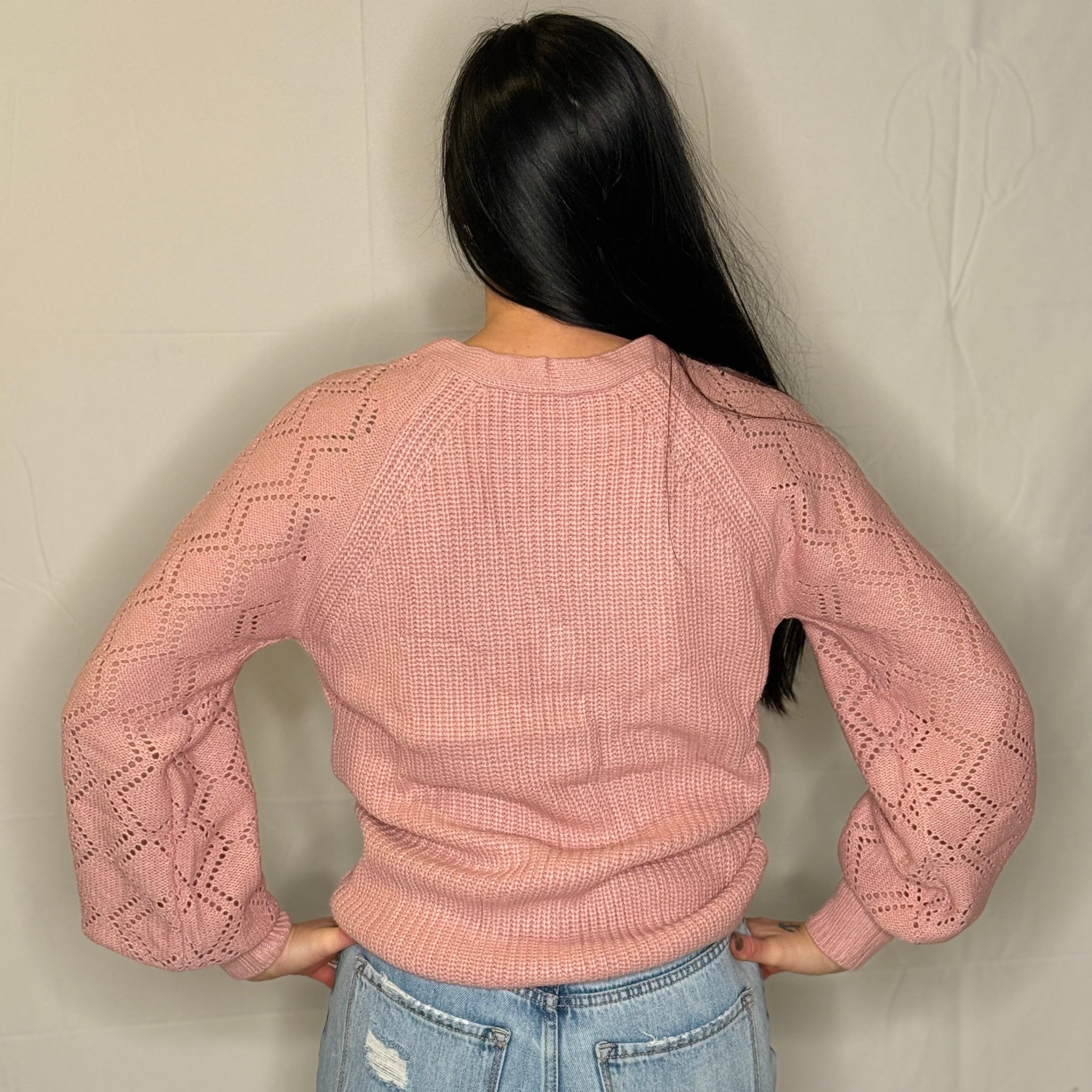 Person wearing a pink knitted sweater and blue jeans against a plain background