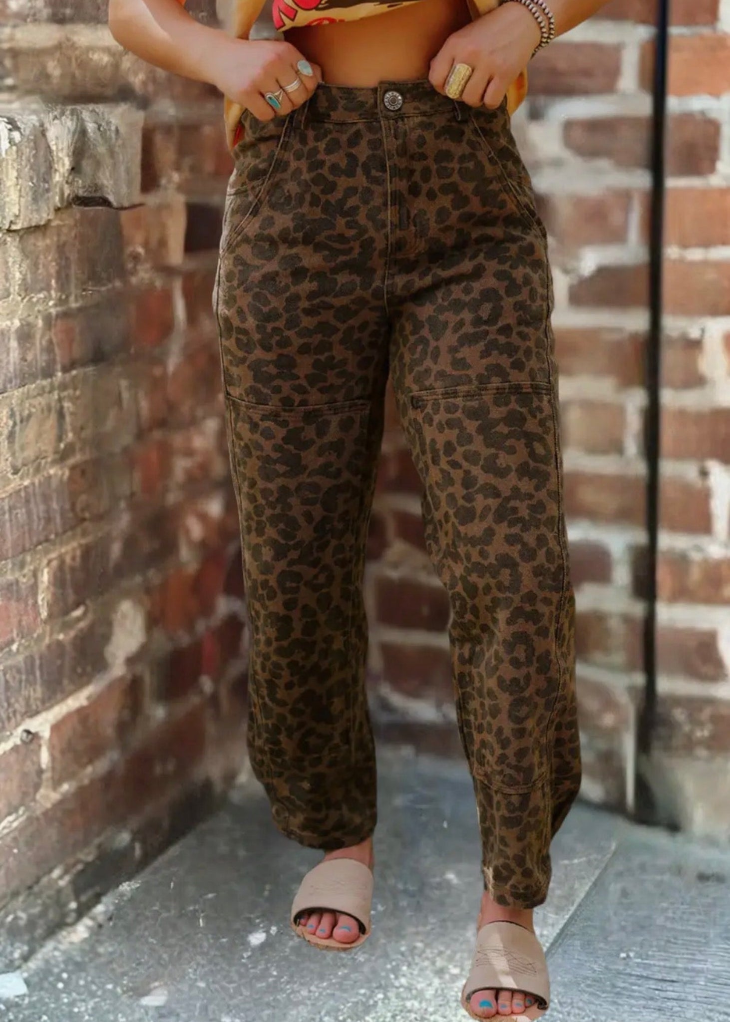 Person wearing leopard print pants and a crop top against a brick wall.
