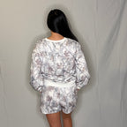 Person wearing a floral outfit with a white belt against a plain background