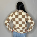 Person wearing a checkered sweater and jeans against a plain background