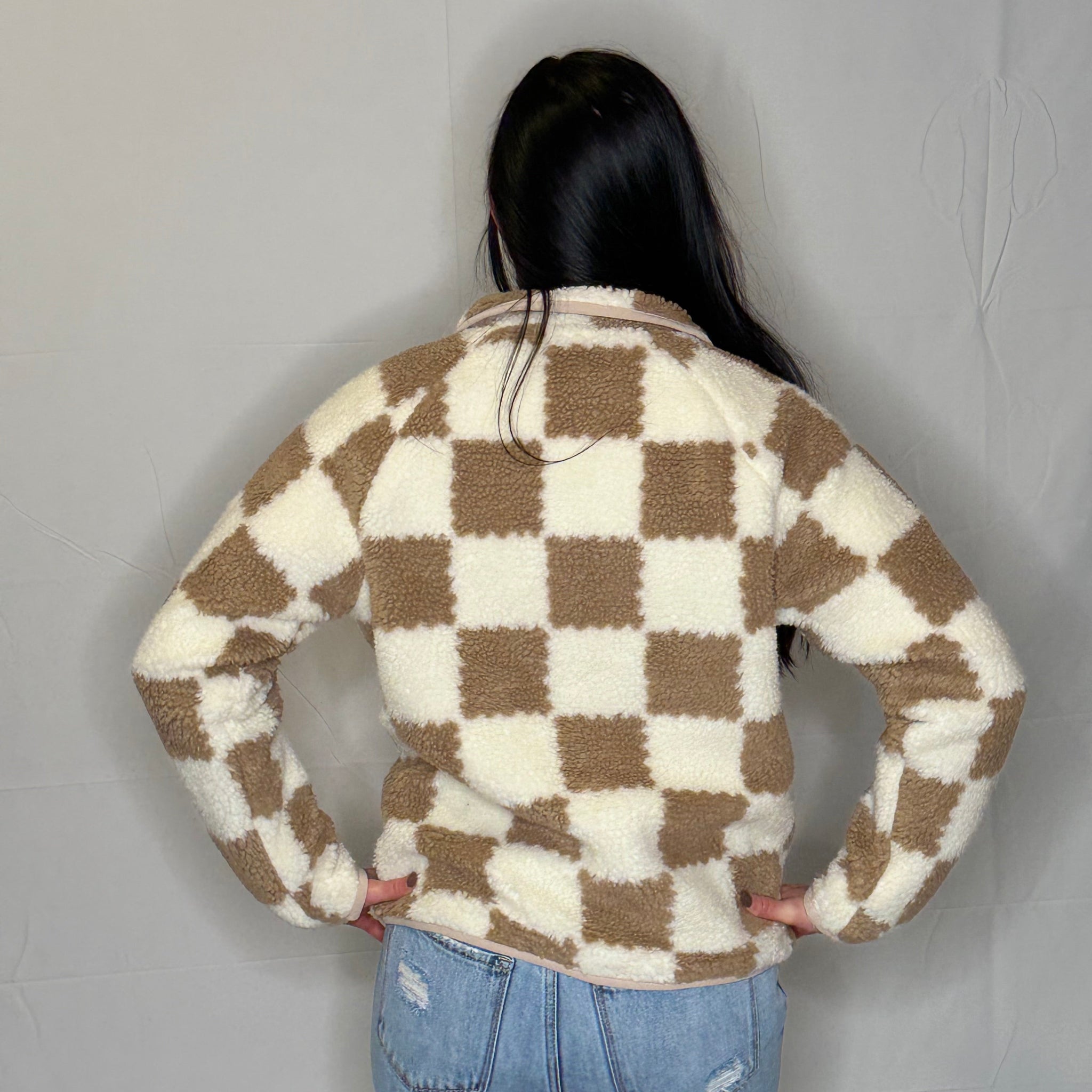 Person wearing a checkered sweater and jeans against a plain background