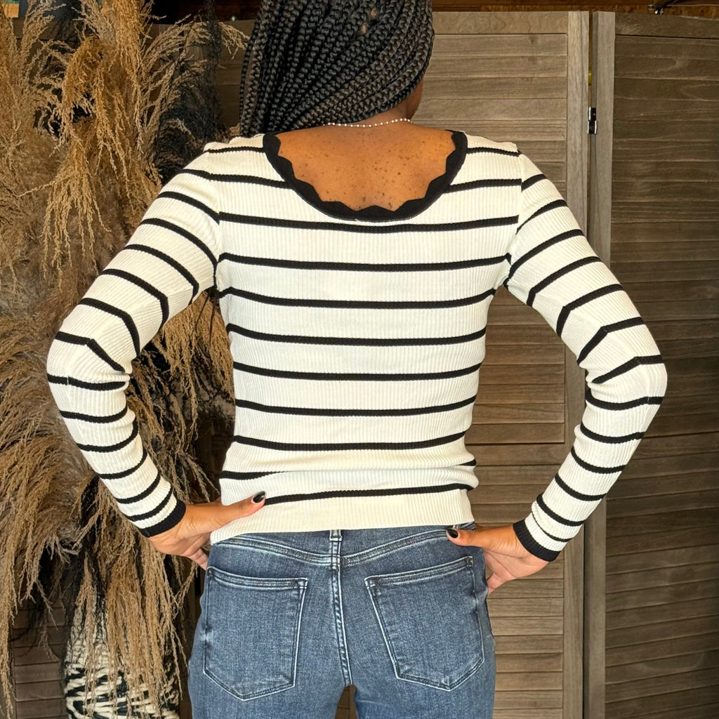 Person wearing a black and white striped sweater and blue jeans with a wooden background