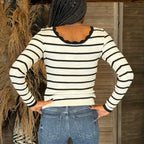 Person wearing a black and white striped sweater and blue jeans with a wooden background
