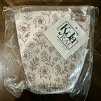 A reusable cloth face mask with a brown floral line-art pattern, sealed in clear plastic packaging with a white paper tag that reads 'Kate Rae Boutique'. The mask is placed on a dark brown wooden floor.