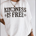White t-shirt with 'Kindness is Free' text and smiley faces on a plain background