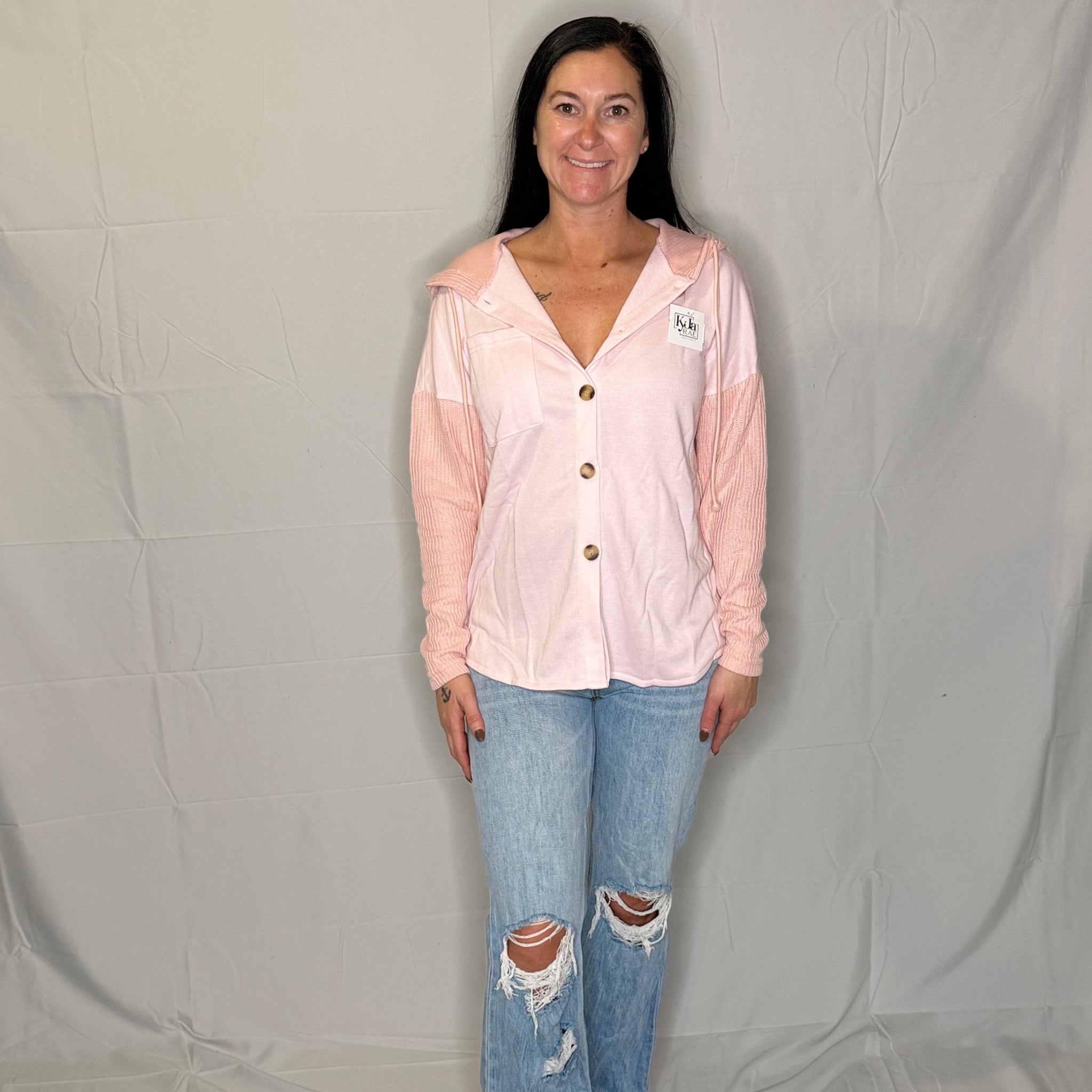 Woman wearing a light pink blouse with buttons and ripped blue jeans on a plain background