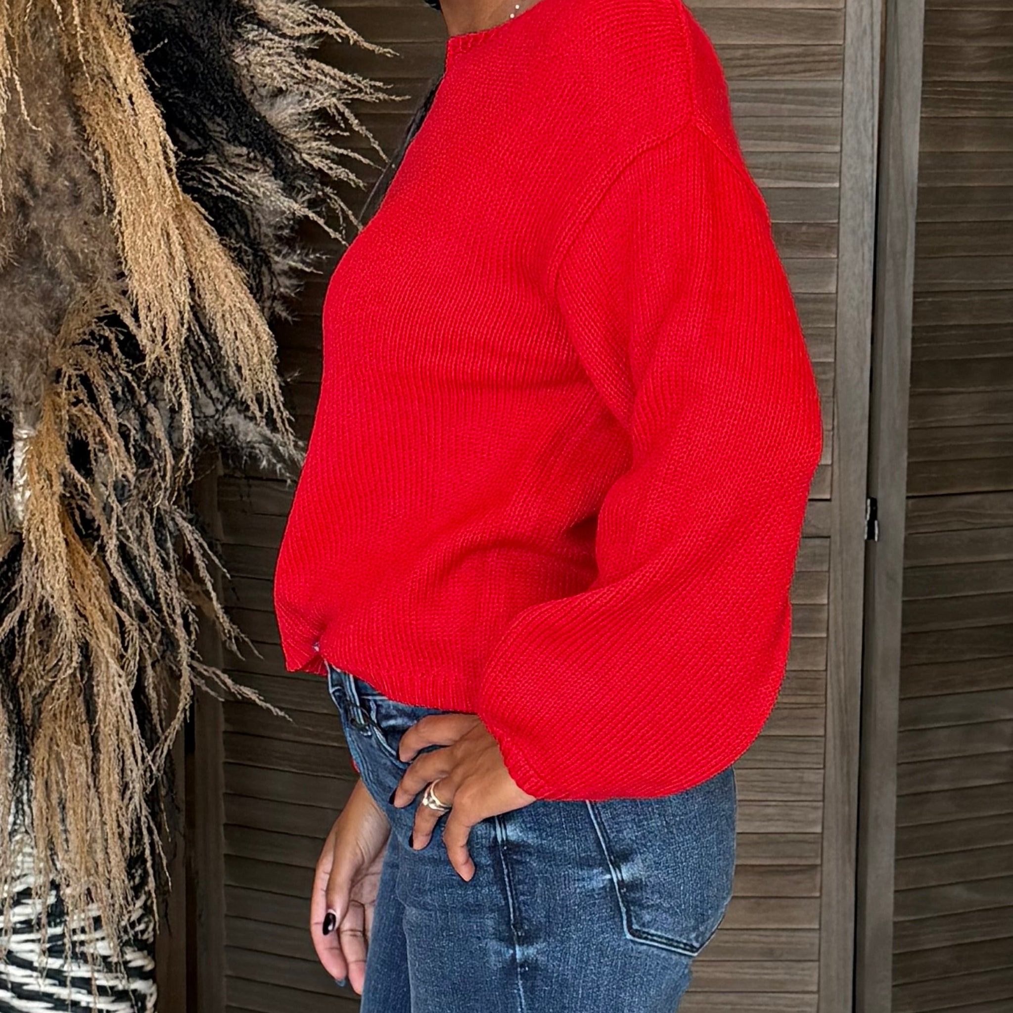 Person wearing a red sweater and blue jeans standing against a wooden wall.