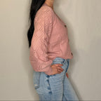 Woman wearing a pink knitted sweater and light blue jeans against a plain background