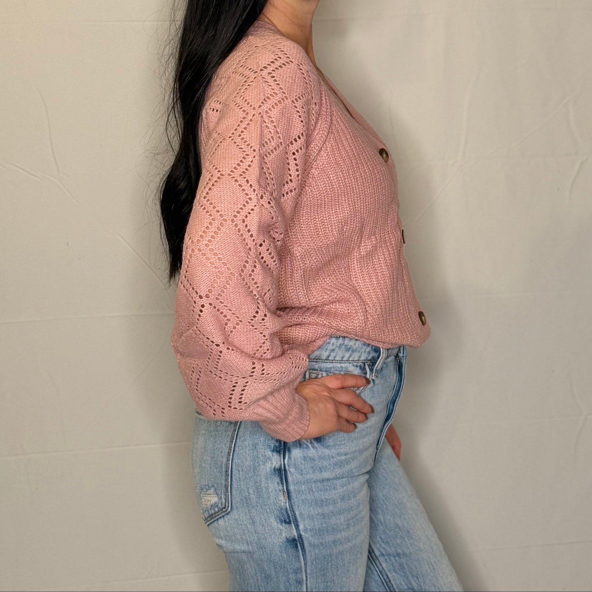 Woman wearing a pink knitted sweater and light blue jeans against a plain background