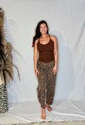 Woman wearing a brown tank top and leopard print pants standing against a white backdrop.