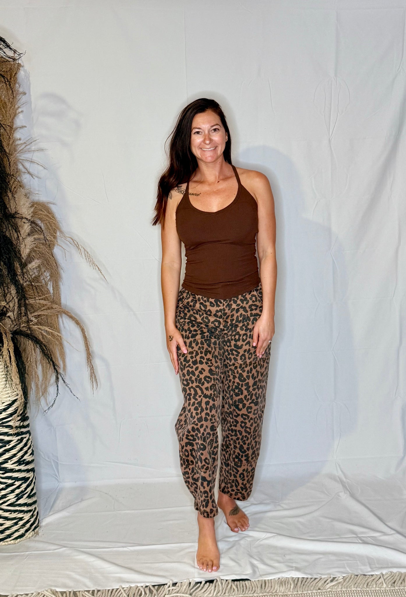 Woman wearing a brown tank top and leopard print pants standing against a white backdrop.