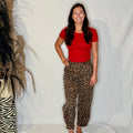 Person wearing a red shirt and leopard print pants standing next to a decorative plant against a white background