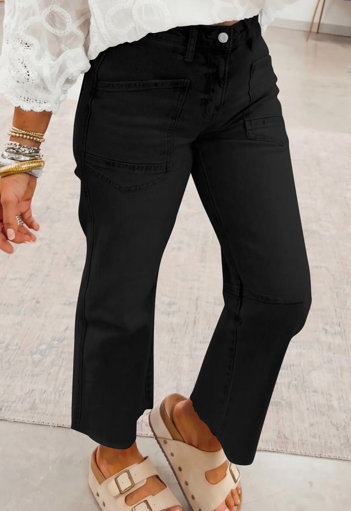 Person wearing black cargo pants with a white lace top and sandals on a light background
