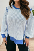 A woman wearing a long-sleeve crewneck top with a blue and white micro-check pattern, solid blue ribbed collar, cuffs, and hem, paired with black pants.