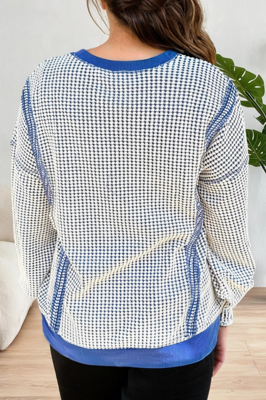 A woman viewed from the back wearing a long-sleeve knit top with a blue and white micro-check pattern and solid blue trim at the collar, cuffs, and hem.