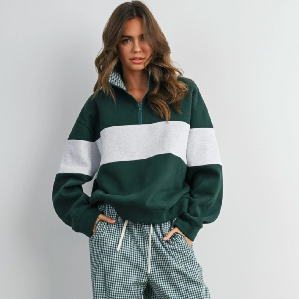A woman modeling a dark green and white color-blocked quarter-zip sweatshirt with matching green-and-white gingham wide-leg pants, standing against a plain light gray wall.