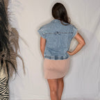 Person wearing a denim vest and beige skirt standing against a plain white background