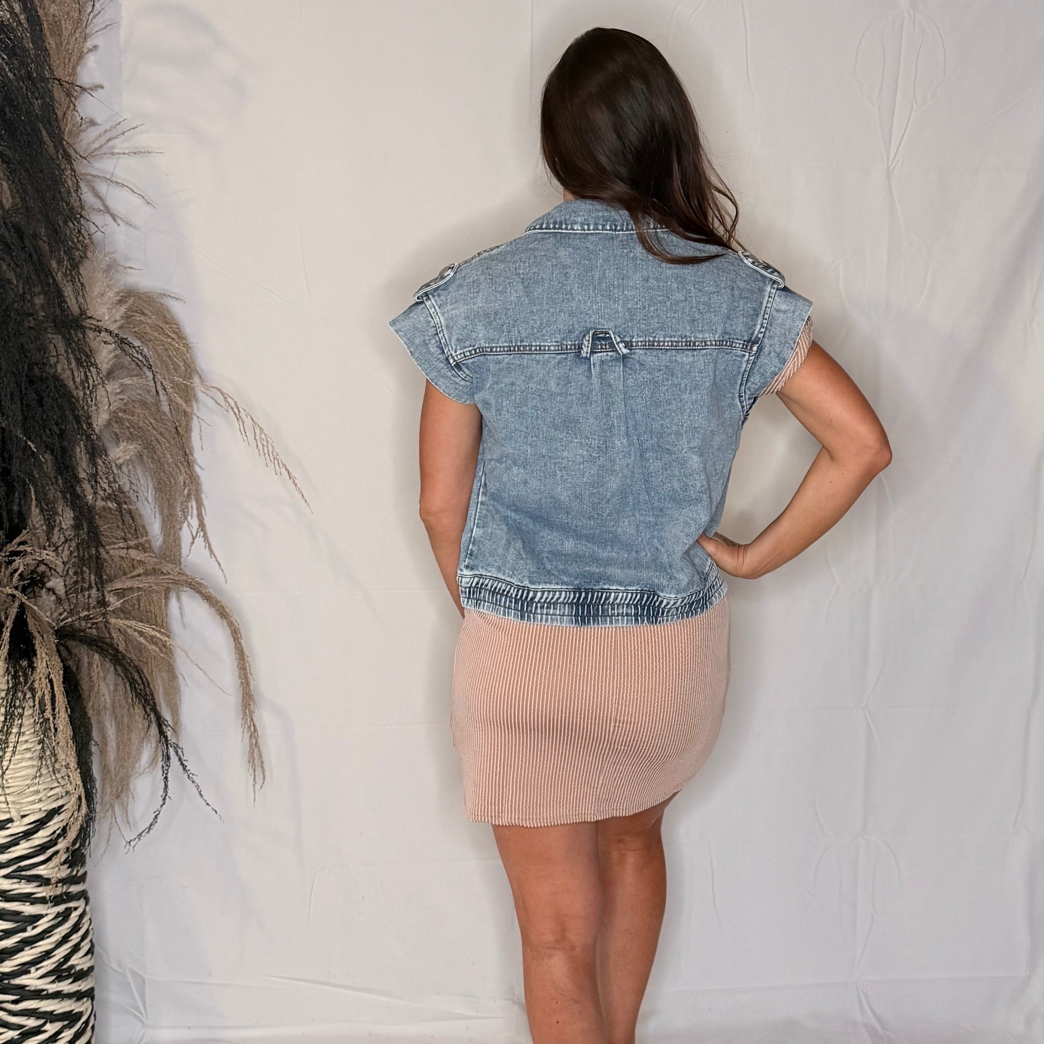 Person wearing a denim vest and beige skirt standing against a plain white background