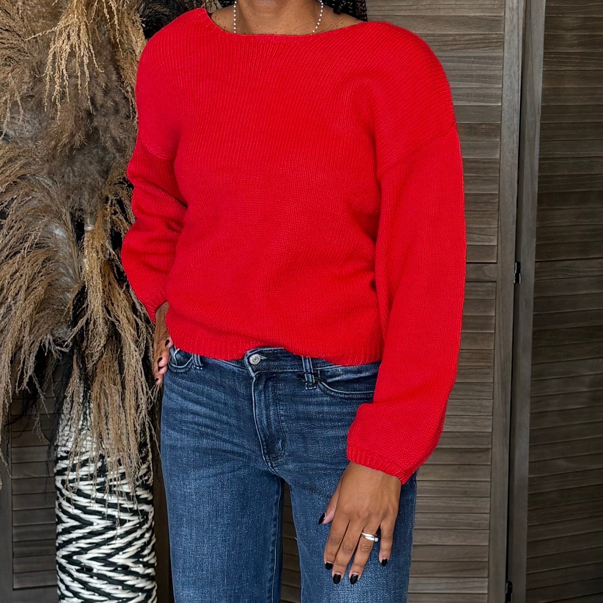 Person wearing a red sweater and blue jeans standing against a wooden wall.