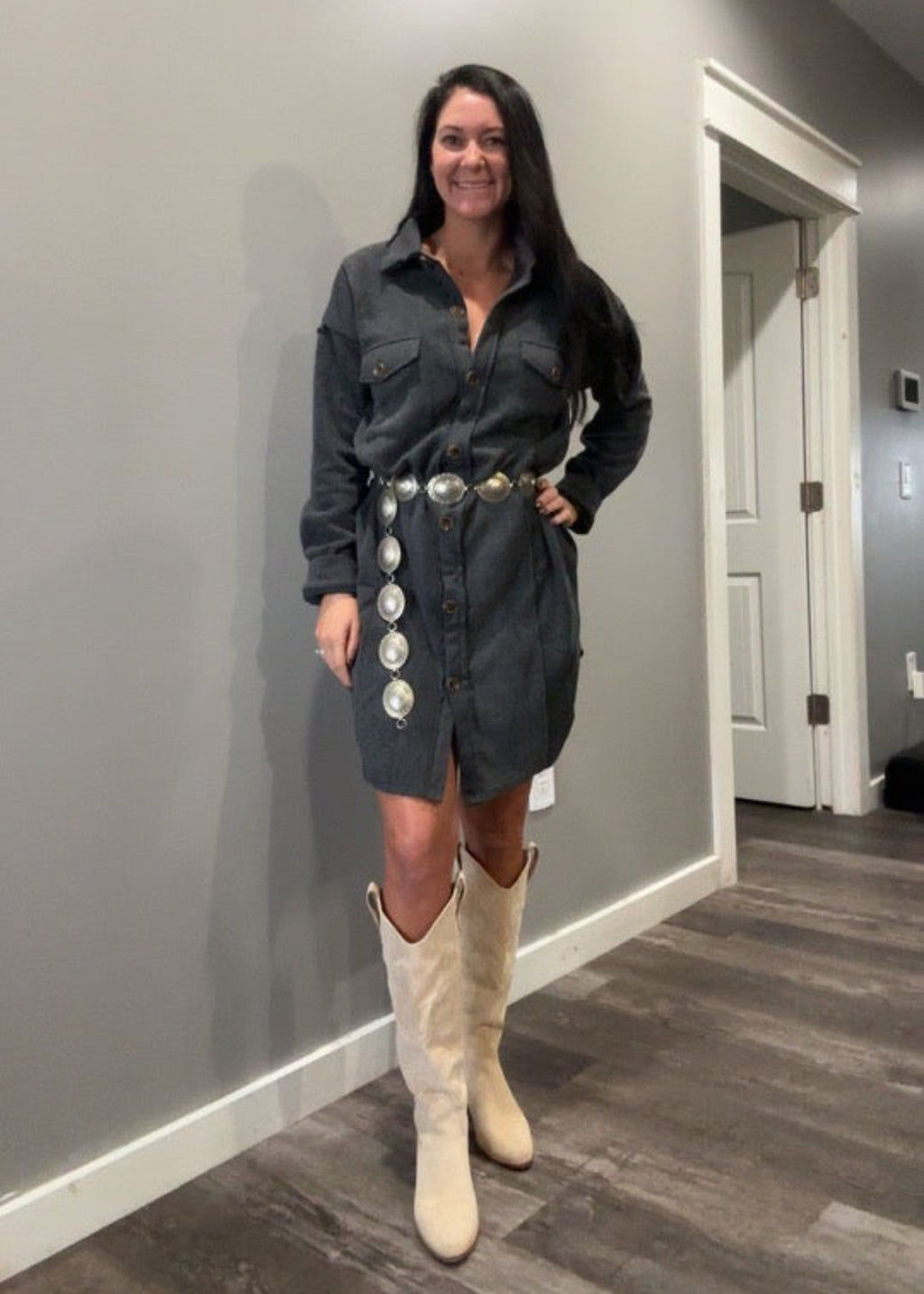 Woman wearing a denim dress with silver buttons and white knee-high boots indoors.
