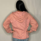 Person wearing a pink jacket and blue jeans against a plain background