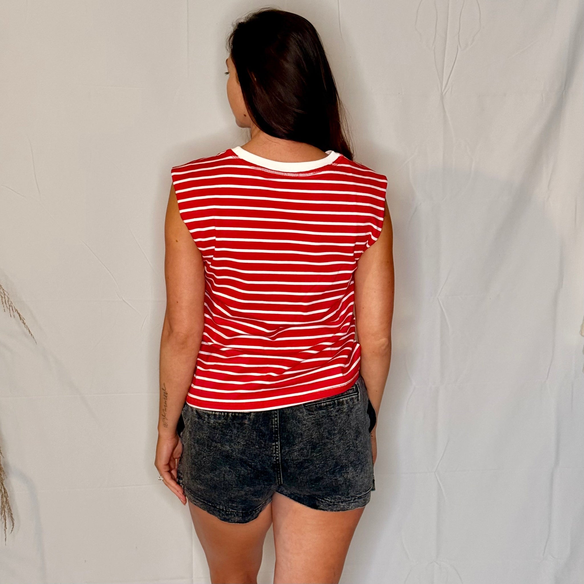 Person wearing a red and white striped tank top and black shorts against a plain background