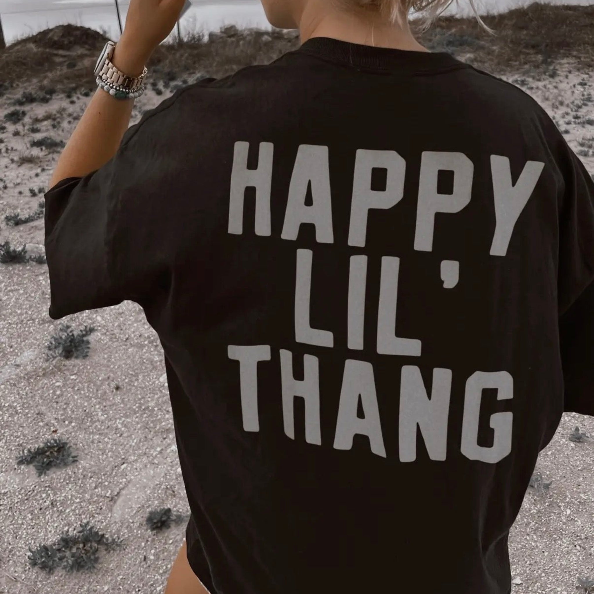 Person wearing a black t-shirt with 'HAPPY LIL THANG' text in a desert setting