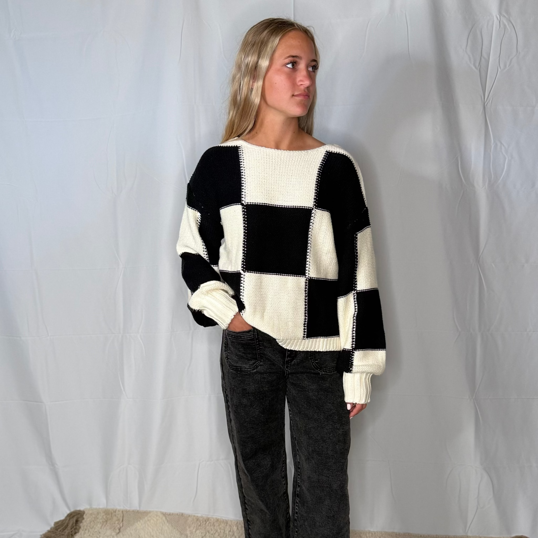Person wearing a black and white checkered sweater with dark pants on a plain background