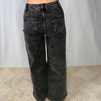 Person wearing black acid-wash jeans against a plain background
