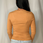 Person wearing a mustard yellow long-sleeve top and light blue jeans against a plain background