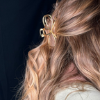 Close-up of a person with wavy hair wearing a gold bow hair clip against a dark background.