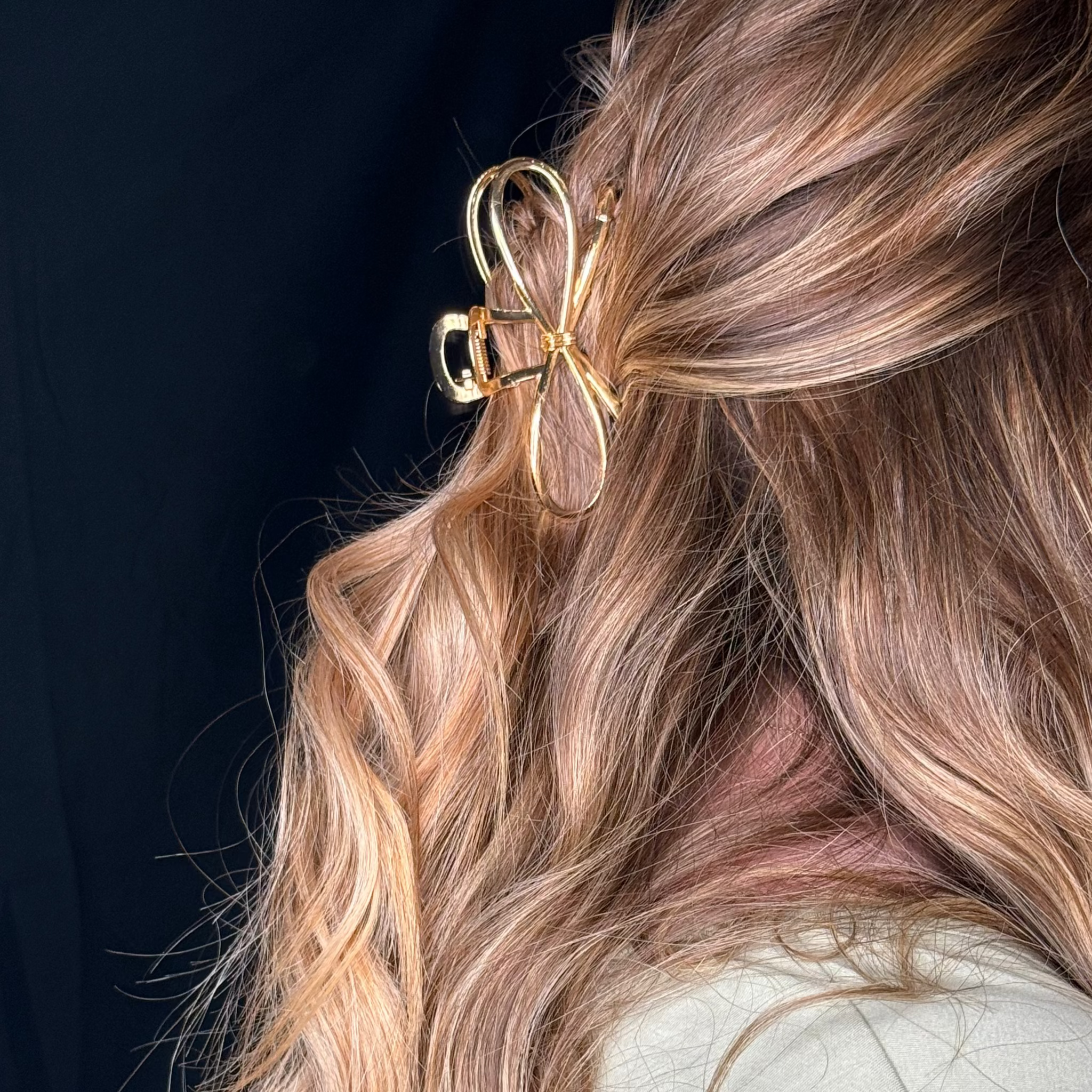 Close-up of a person with wavy hair wearing a gold bow hair clip against a dark background.