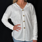 Woman wearing a light gray hoodie with buttons on a black background