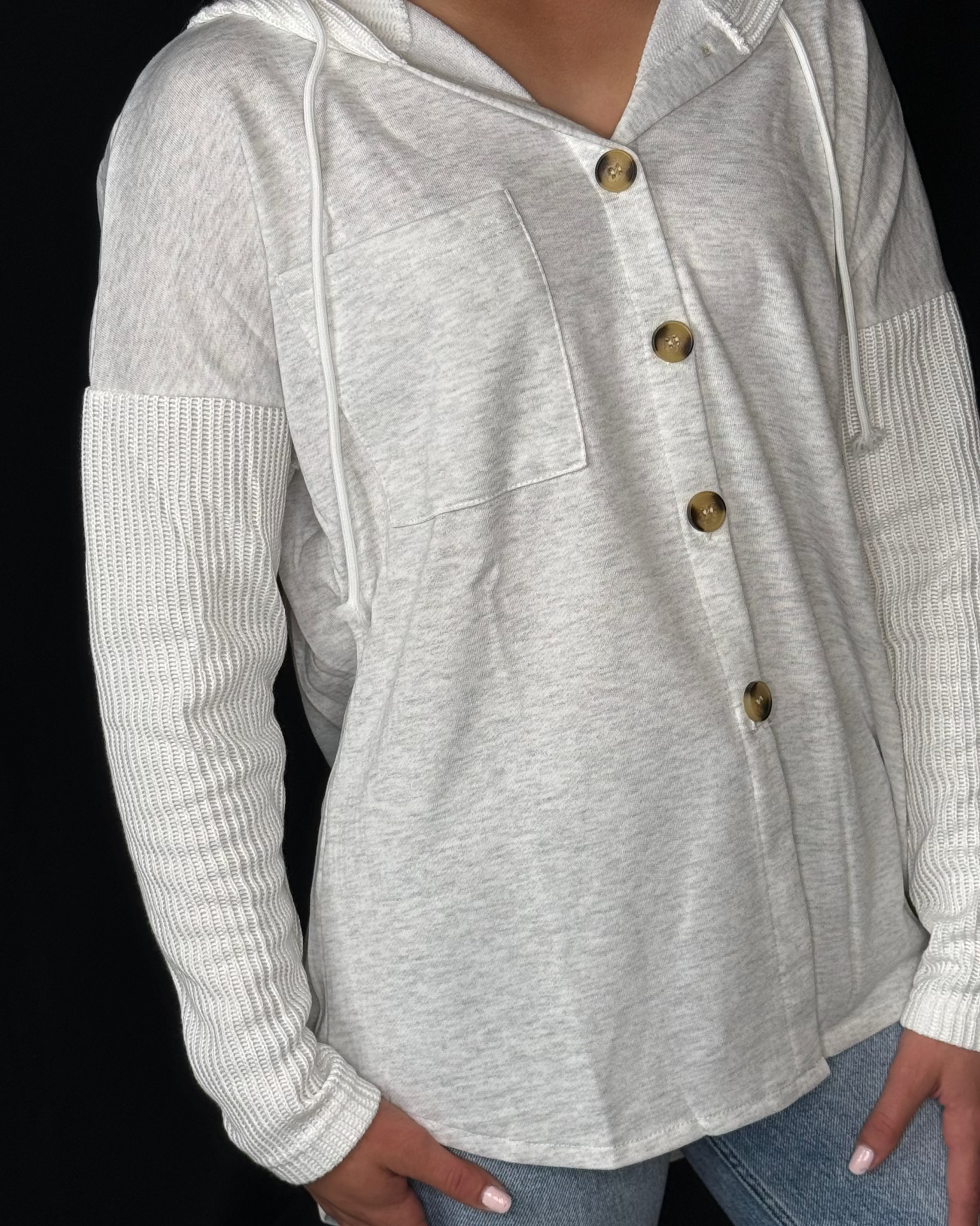 Gray hoodie with button details worn by a person on a black background