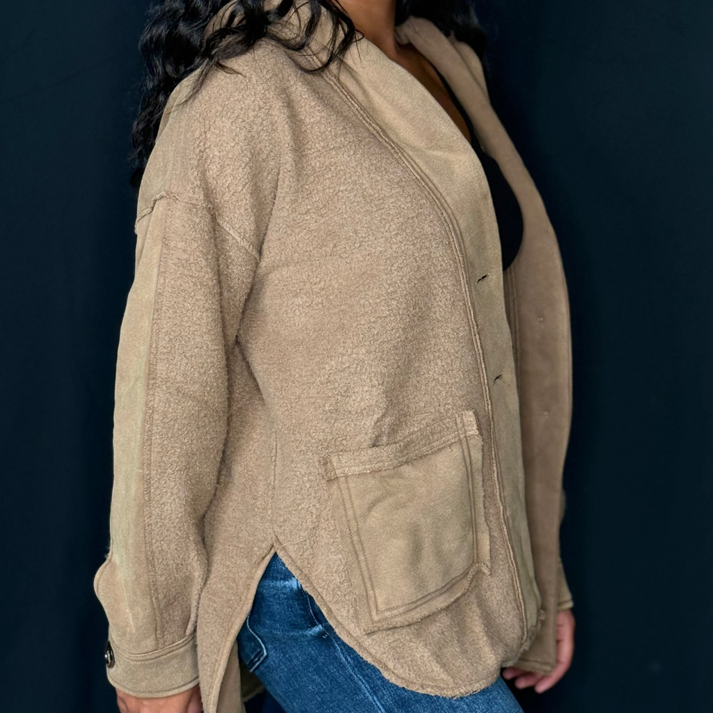 Person wearing a beige jacket and blue jeans against a dark background