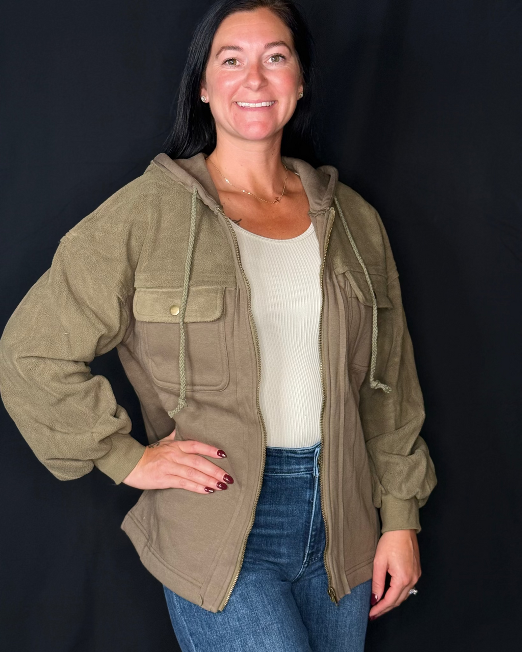 Woman wearing a green jacket over a white shirt and blue jeans on a black background