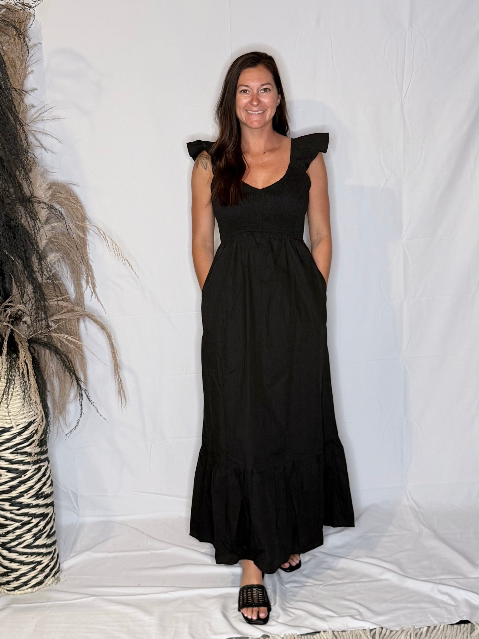 Woman wearing a black dress standing against a white background with decorative elements.
