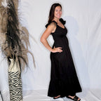 Woman in a black dress standing next to a decorative plant against a white background