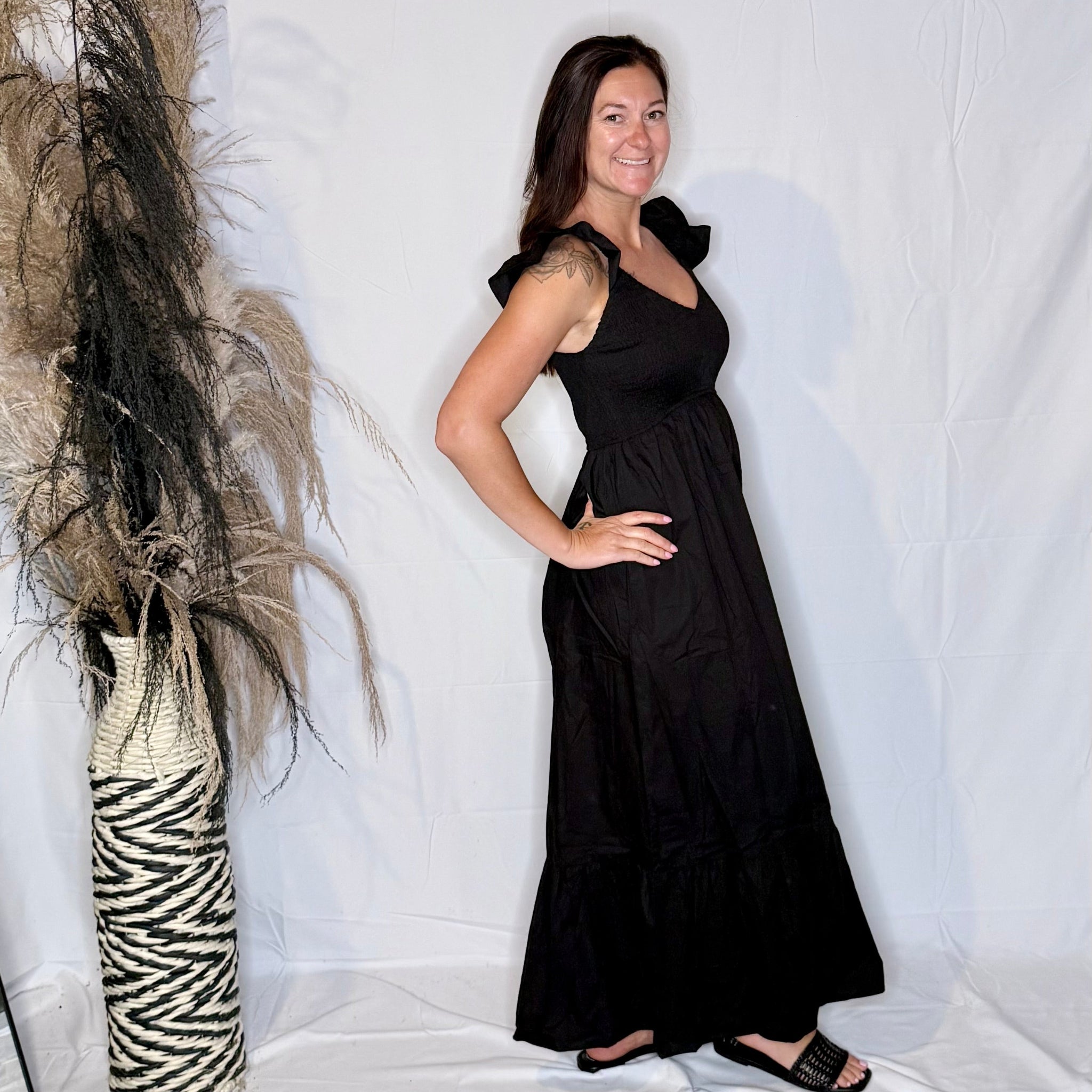 Woman in a black dress standing next to a decorative plant against a white background