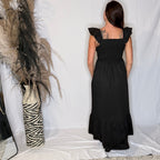Person wearing a black dress standing in front of a white curtain with decorative elements.