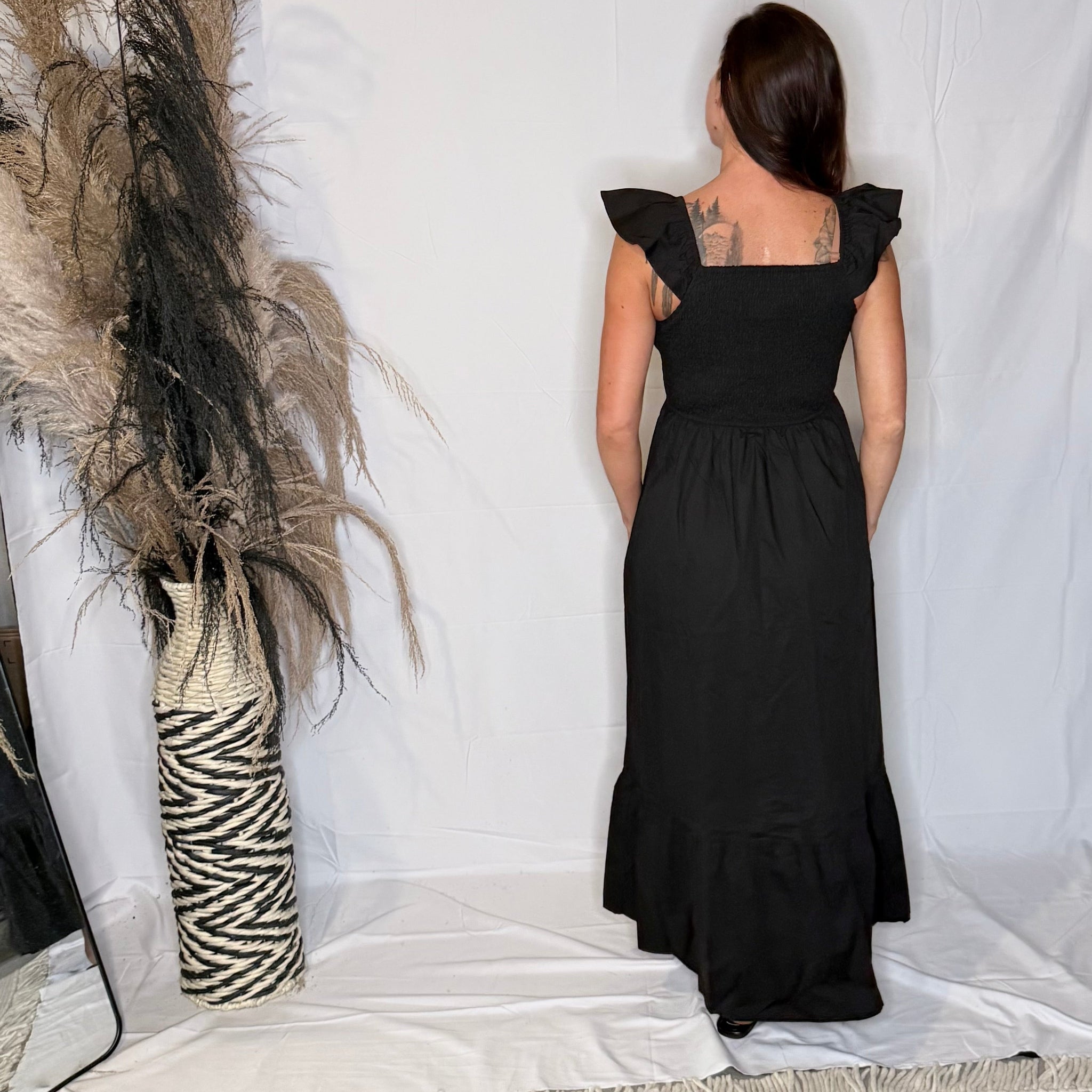 Person wearing a black dress standing in front of a white curtain with decorative elements.