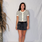 Woman wearing a black and white striped shirt and denim skirt standing against a plain background