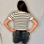 Person wearing a black and white striped shirt and denim shorts against a plain background