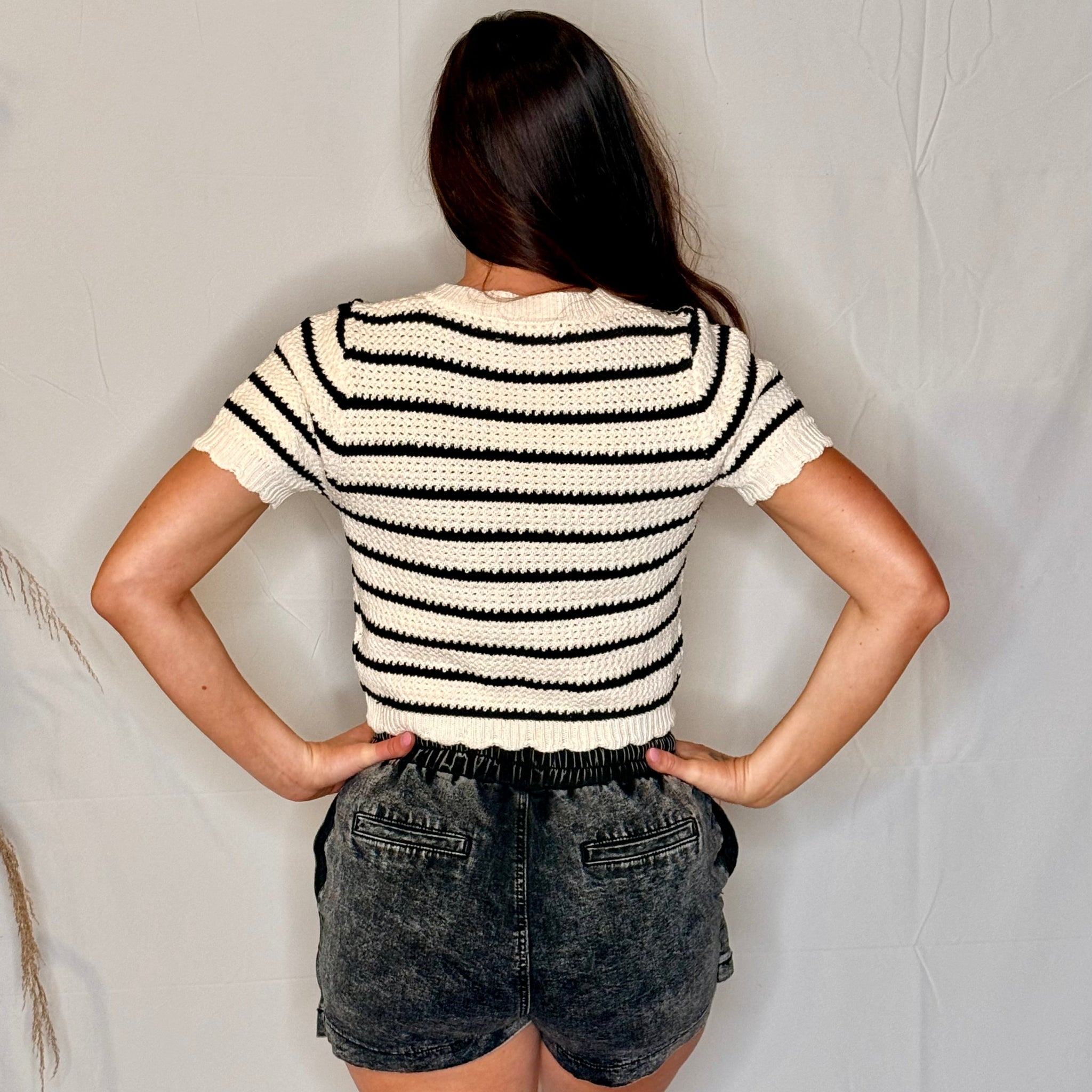 Person wearing a black and white striped shirt and denim shorts against a plain background